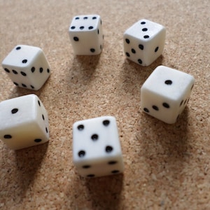 Peut inclure: Six dés blancs avec des points noirs sur un fond de liège. Les dés sont disposés en cercle avec un dé au centre.
