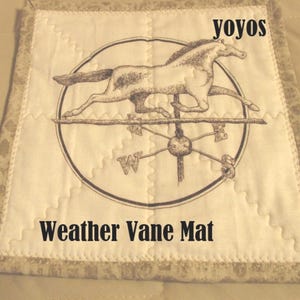 May include: A square, quilted weather vane mat with a beige background and a decorative border. The mat features a black and white illustration of a running horse atop a weather vane. The text "yoyos" and "Weather Vane Mat" are printed on the mat.