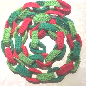 May include: A crocheted chain in a spiral arrangement. The chain links are in alternating colors of red, green, and light green. The handmade chain is likely for decorative purposes.