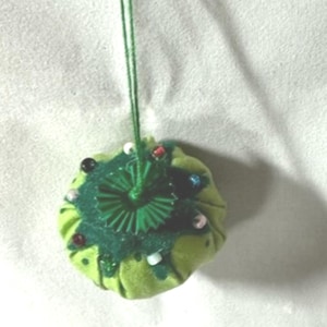May include: A green pincushion shaped like a Christmas tree with a green ribbon and colorful beads.