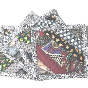 May include: Three square fabric coasters with a patchwork design. The coasters are made of different fabrics in various colors and patterns, including black, white, red, green, and purple. The coasters have a black and white zebra print border.