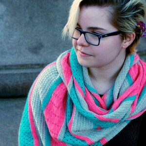 May include: A woman wearing a gray, pink, and turquoise knitted scarf with a geometric pattern. The scarf is draped around her neck and shoulders.