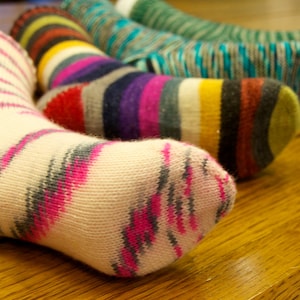 Könnte beinhalten: Vier Paar bunte gestreifte Socken, mit einem Paar in rosa und grauen Streifen, einem Paar in rot, weiß und blauen Streifen, einem Paar in lila, weiß und schwarzen Streifen und einem Paar in grün und blauen Streifen.