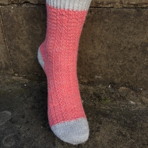 May include: A pair of knitted socks in a pink and grey colour scheme. The socks are made with a textured stitch pattern.