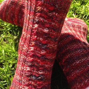 May include: A pair of red, pink and purple knitted socks with a textured pattern. The socks are made with a variety of yarns and have a unique, hand-crafted look.