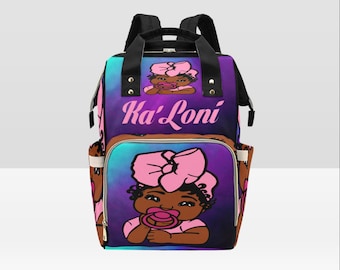May include: A black diaper bag with a purple, blue, and pink galaxy print. The bag has a large pocket on the front with a pink bow and a cartoon image of a Black baby girl with a pacifier. The bag is personalized with the name "Ka'Loni" in pink letters.