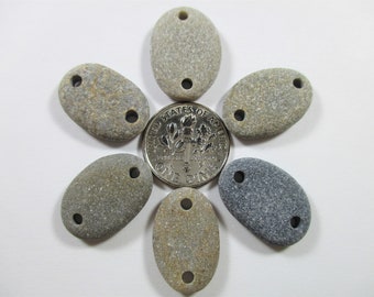 May include: Six smooth, oval-shaped stones with two holes drilled through each. The stones are various shades of brown and gray. A US dime is included for scale.