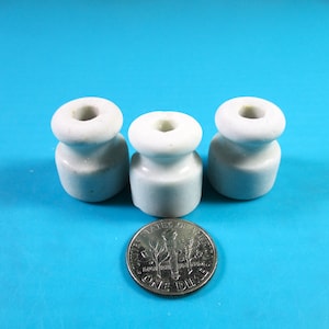 May include: Three small, white ceramic insulators with a rounded top and base, and a hole through the center. A dime is placed in front of the insulators for size comparison. The insulators are on a bright blue background.