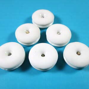 May include: Six white ceramic buttons with a small hole in the center. The buttons are arranged in a triangular pattern on a blue background.