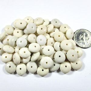 May include: A pile of off-white, round beads with a hole in the center. A US dime is next to the beads for size comparison. The beads are smooth and appear to be made of a natural material.