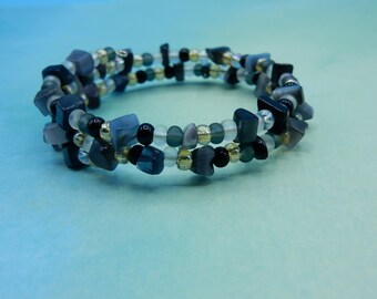 May include: A multi-strand bracelet featuring black, grey, and white beads. The bracelet is made from small, irregularly shaped beads.