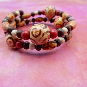 May include: A triple-strand wooden bead bracelet with brown, white, and red beads. The beads have a floral pattern.