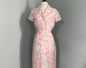 Könnte beinhalten: Ein weißes Kleid mit einem rosa-blauen Blumenmuster. Das Kleid hat einen Kragen, kurze Ärmel und eine figurbetonte Silhouette.