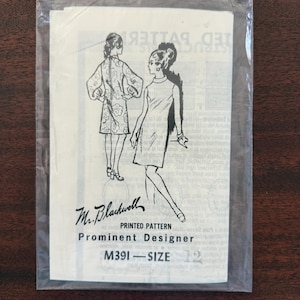 Puede incluir: Un patrón de costura vintage en una funda de plástico transparente. El patrón presenta ilustraciones de dos mujeres con vestidos. El texto "Mr. Blackwell Printed Pattern Prominent Designer M391 - SIZE 12" está impreso en el patrón.