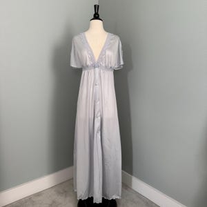 May include: A light blue vintage nightgown on a mannequin. The gown features a V-neckline with lace trim, short sleeves, and a button-down front. The empire waist is gathered, and the gown falls to the floor.