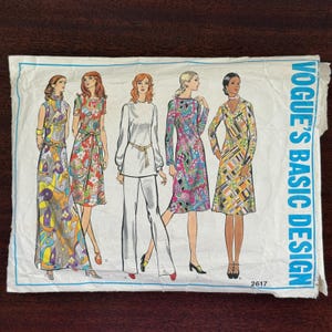 May include: Vintage Vogue's Basic Design sewing pattern featuring five different 1970s fashion designs. The illustrations include a long dress, a wrap dress, a pantsuit, and two other dresses, all with vibrant patterns and colors. The pattern number is 2617.