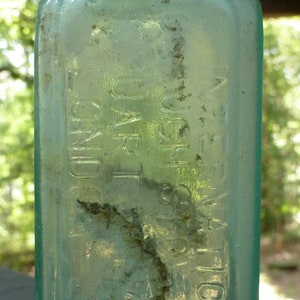 Puede incluir: Una botella vintage de vidrio transparente con una superficie texturizada. La botella tiene un cuello estrecho y una base ancha. La botella está etiquetada con el texto "DR. BULL'S" y "Sarsaparilla".
