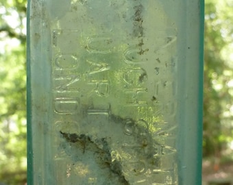Puede incluir: Una botella vintage de vidrio transparente con una superficie texturizada. La botella tiene un cuello estrecho y una base ancha. La botella está etiquetada con el texto "DR. BULL'S" y "Sarsaparilla".