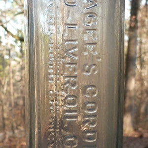 May include: A clear glass bottle with a label that reads "Hage's Cordial Cod Liver Oil Compound".