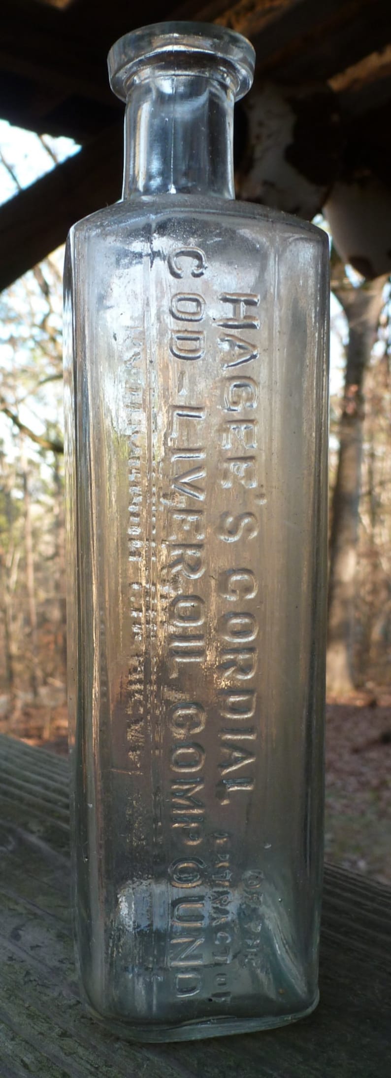 May include: A clear glass bottle with a label that reads "Hage's Cordial Cod Liver Oil Compound".