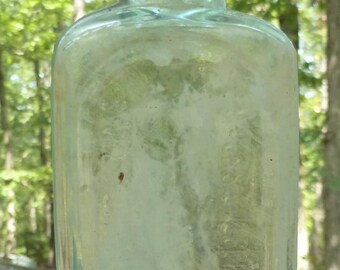 Puede incluir: Una botella de vidrio transparente con una superficie redonda y texturada. La botella tiene una boca ancha y un cuello corto.