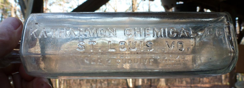 May include: A clear glass bottle with the text "KATHARMON CHEMICAL CO. ST. LOUIS, MO." embossed on the front.
