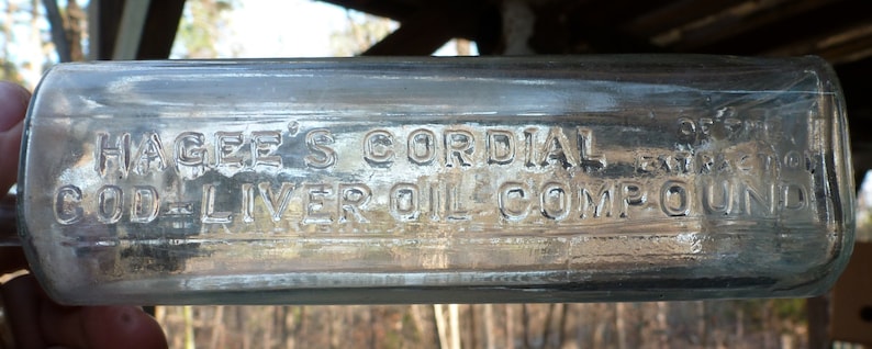 May include: A clear glass bottle with a label that reads "Hagee's Cordial 32% Extra Strong Cod Liver Oil Compound".