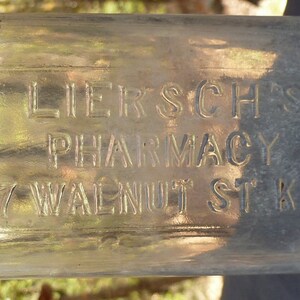 May include: A clear glass bottle with the text "Liersch's Pharmacy 307 Walnut St. K.C. Mo." etched into the side.