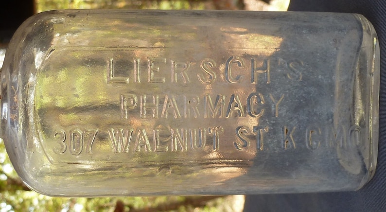 May include: A clear glass bottle with the text "Liersch's Pharmacy 307 Walnut St. K.C. Mo." etched into the side.