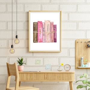 May include: A framed watercolor print of a stack of books in shades of pink, brown, and purple, tied with twine. The books are displayed on a desk with a wooden chair, a small plant, and a clock. The background is a white brick wall.