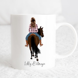 May include: White ceramic mug featuring a colourful illustration of a person riding a brown horse. The text "Lilly & Magic" is printed on the bottom of the mug.