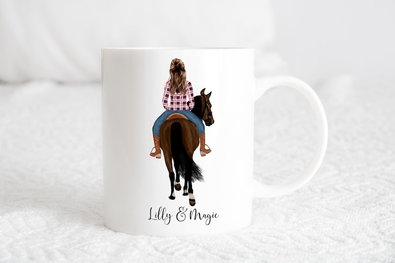 May include: White ceramic mug featuring a colourful illustration of a person riding a brown horse. The text "Lilly & Magic" is printed on the bottom of the mug.