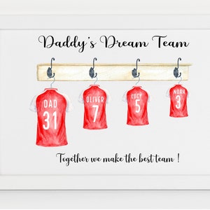 May include: A white framed print with the text "Daddy's Dream Team" and four red soccer jerseys hanging on a wooden rack. The jerseys have the names "Dad", "Oliver", "Lucy", and "Noah" and numbers 31, 7, 5, and 3 on them. The text "Together we make the best team!" is at the bottom of the print.