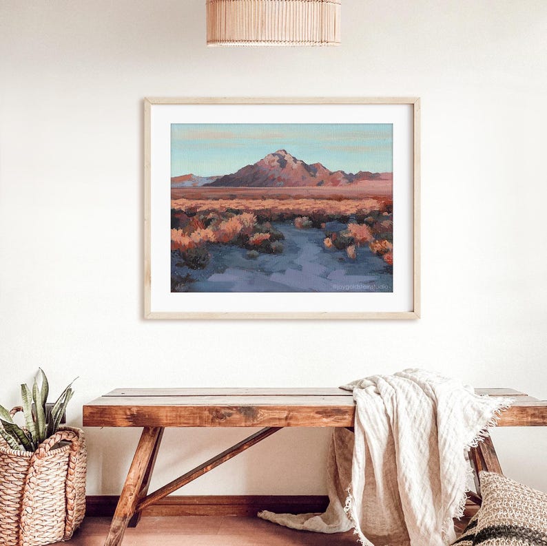 A natural cozy entry way with a wooden bench and potted plant interior. A large Nevada landscape art print is framed showing an original painting of Sunrise Mountain in Las Vegas.