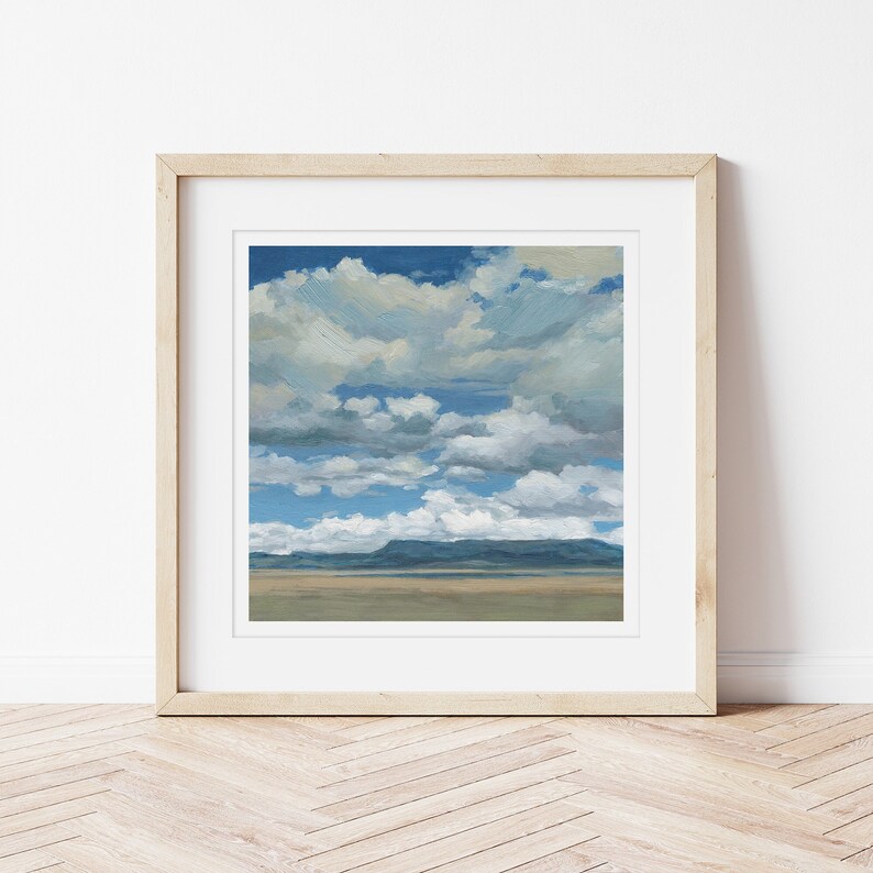 Art print of blue sky and white clouds over a desert mesa. Framed in a light maple wood frame.