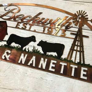 May include: A copper metal sign with a farmhouse theme. The sign features a red barn, two black cows, a windmill, and the text "Beckwith Est. 1973 Josh & Nanette".