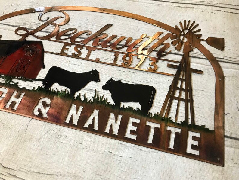 May include: A copper metal sign with a farmhouse theme. The sign features a red barn, two black cows, a windmill, and the text "Beckwith Est. 1973 Josh & Nanette".