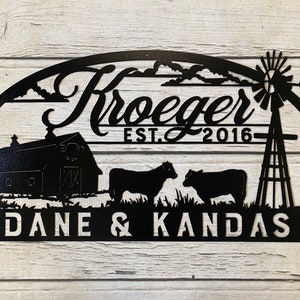 May include: Black metal sign with a farmhouse theme. It features a barn, two cows, a windmill, and the text "Kroeger EST. 2016" and "DANE & KANDAS".