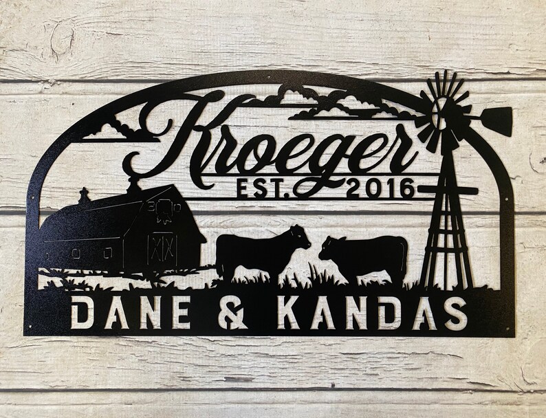 May include: Black metal sign with a farmhouse theme. It features a barn, two cows, a windmill, and the text "Kroeger EST. 2016" and "DANE & KANDAS".