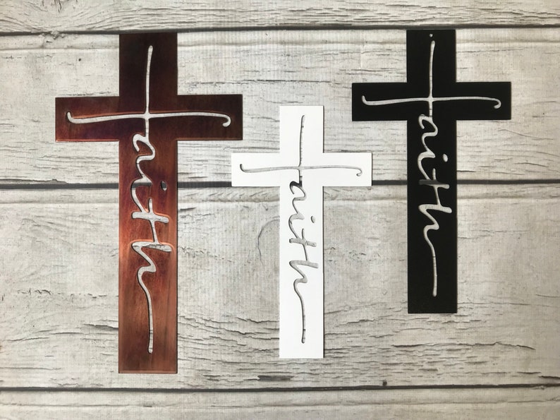 Puede incluir: Tres cruces decorativas en marr&oacute;n, blanco y negro. Cada cruz presenta la palabra "faith" recortada en una fuente cursiva. Las cruces se muestran sobre un fondo claro de vetas de madera.