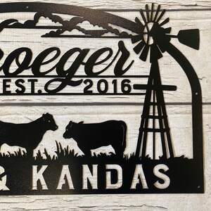 May include: Black metal sign with the text "Froeger Est. 2016" and "& KANDAS" with a silhouette of a windmill, two cows, and grass.
