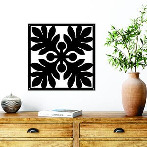 May include: Black metal wall decor with a geometric design featuring four stylized leaves. The decor is hanging on a white wall above a wooden dresser with two drawers.