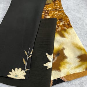 Peut inclure: Trois pièces de tissu pliées. La première est noire avec un motif floral, la seconde est vert foncé avec un motif de feuille, et la troisième est ornée de motifs jaunes, bruns et crème. Les tissus semblent être de la soie ou un matériau similaire.