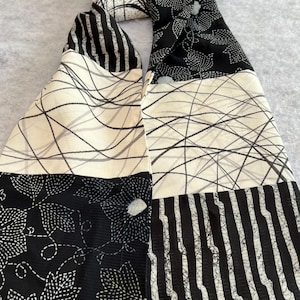 Pode incluir: Lenço estampado em preto e branco com riscas, motivos florais e linhas abstratas. O lenço é feito de um tecido macio e está dobrado sobre si mesmo. O design do lenço é visível.