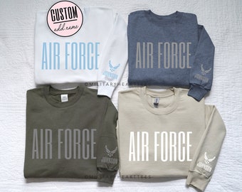 May include: Four long-sleeved sweatshirts in different colors: white, blue, green, and beige. Each sweatshirt has the text "AIR FORCE" printed in gray on the front and a blue Air Force logo with the word "JOHNSON" printed on the sleeve.