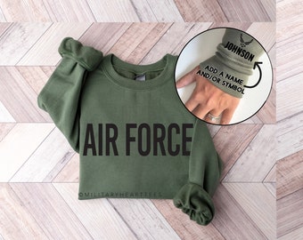 May include: A green sweatshirt with the words "AIR FORCE" printed on the front. The sleeve has a space to add a name and/or symbol. The text on the sleeve reads "JOHNSON".