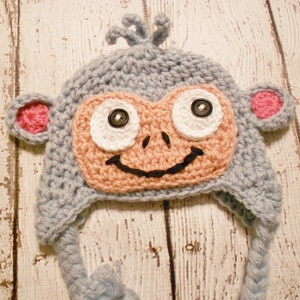 May include: A crocheted monkey hat with blue and pink yarn, featuring large white eyes with black pupils and a black smile.