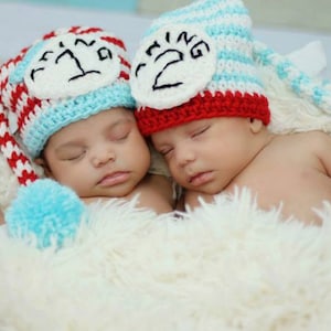 Puede incluir: Dos bebés con gorros de punto rojo y azul con las palabras "Thing 1" y "Thing 2" en ellos. Los bebés están durmiendo en una manta blanca y esponjosa.