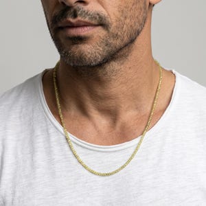 May include: A necklace composed of small, faceted, translucent yellow-green beads strung together in a continuous circular chain. The beads have a reflective, sparkling quality and are uniform in size, resting against a plain white t-shirt.
