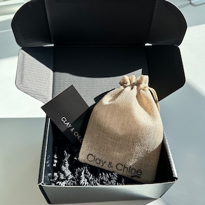 Clay and Chloe Jewelry Packaging - Black box with crinkle paper at the bottom. A business card with Clay & Chloe. A Clay & Chloe hand stamped burlap pouch that the jewelry will go into. Then the box will be shipped in a water proof poly mailer.